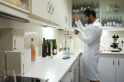 Arabic winemaker working in winelab wearing white gown and gloves.