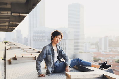 Full length side view portrait of young woman sitting in city