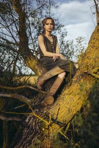 Woman sitting on a tree in boots and a long dress