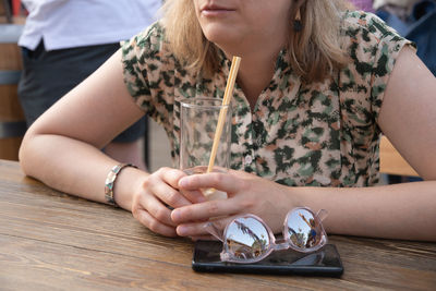 Unrecognizable young woman holding glass with cold exotic cocktail, sitting at table in street cafe 