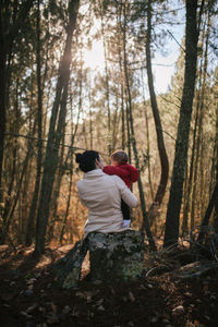 Rear view of mother carrying daughter while standing amidst trees at forest