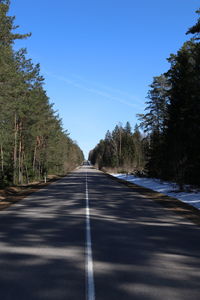 Empty road along trees and plants against sky