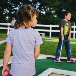 Rear view of girl with brother playing miniature golf at lawn