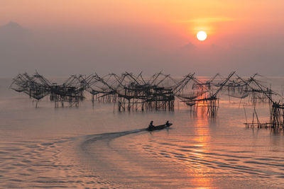 Huts in sea against sky during sunset