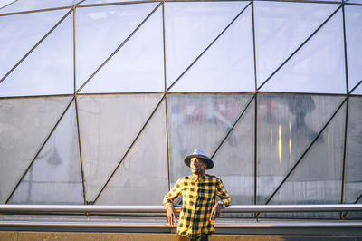 Thoughtful african man looking away while standing against glass building