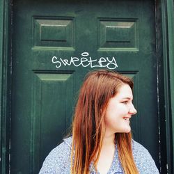 Close-up of smiling woman looking away against door