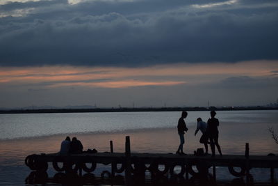 Silhouette people by sea against sky during sunset