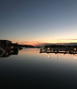 Illuminated city by river against sky during sunset