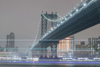 Illuminated bridge over river against sky in city at night