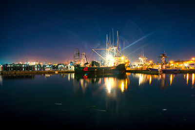 Illuminated cranes at harbor against sky at night