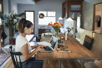 Side view of woman working on laptop at dining table