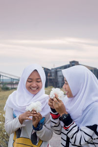 Close-up of happy female friends holding white flowers on field