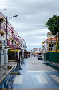 Empty road by buildings in city against sky