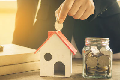 Midsection of businesswoman holding coin over model house