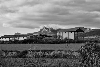 Abandoned house on field by buildings against sky