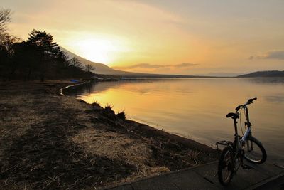 Bicycle by lake against sky and snowcapped volcano during sunset