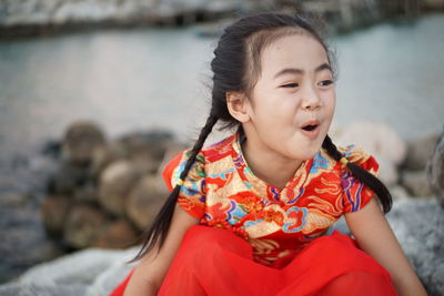 Smiling cute girl shouting while sitting on rocks against sea