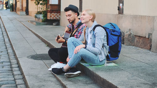 Full length of young man using mobile phone while sitting on footpath