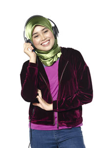 Happy young woman wearing velvet jacket listening music through headphones against white background