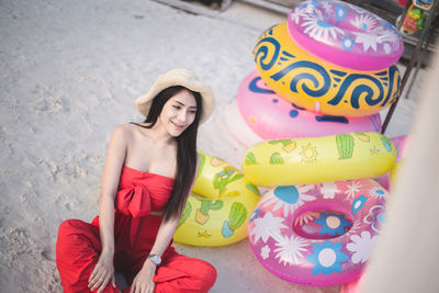 Young woman sitting by inflatable rings at shore of beach