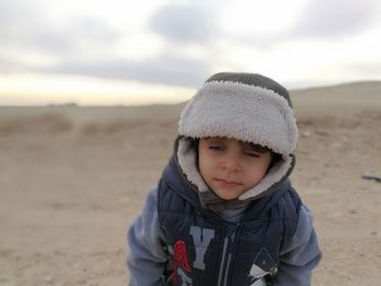 Boy wearing hunter hat at desert against sky