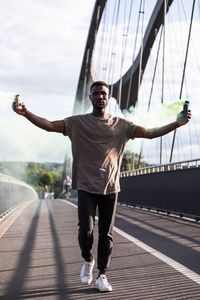 Full length of young man with arms raised against sky