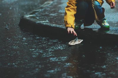 Low section of girl with paper boat on road during rain