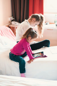 Girl watching video in digital tablet by sister on bed at home