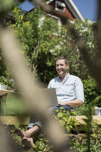 Happy mid adult man with laptop relaxing on terrace