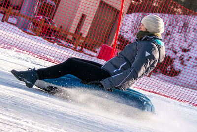 Side view of young woman on sled at snow field