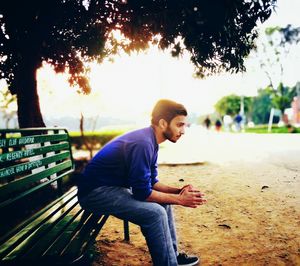 Young man using mobile phone while sitting on tree