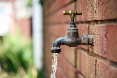 Close-up of water running from faucet at brick wall