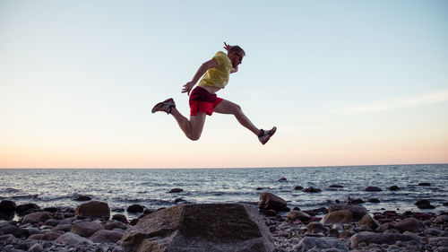 Man jumping at beach against sky during sunset