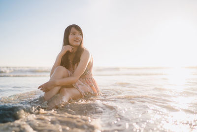 Woman sitting on beach against clear sky