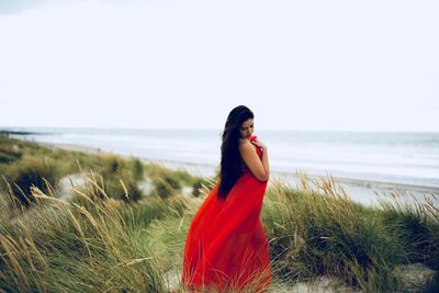 Young woman standing on beach against sky