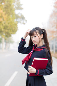 Woman holding book while standing on road