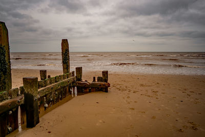 Wooden posts on beach against sky