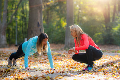 Woman doing push-ups, personal fitness trainer looking at a smart watch during training in the park.