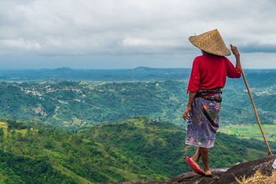 Rear view of man standing on mountain against sky