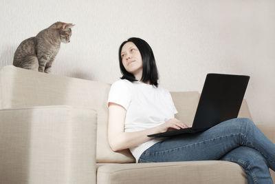 Full length of woman using mobile phone while sitting on sofa