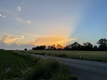 Road amidst field against sky during sunset