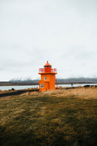 Lighthouse on field by building against sky