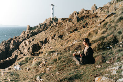 Rear view of man sitting on rock against sky