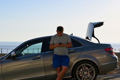 Rear view of man leaned on the car