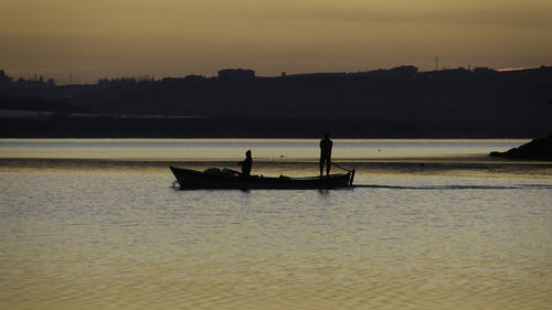 Silhouette people in boat on sea against sky during sunset