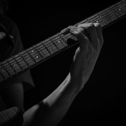 Midsection of man playing guitar against black background