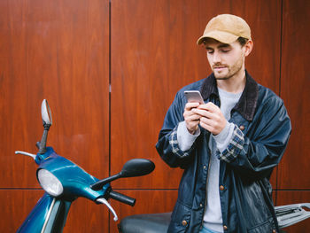 Portrait of young man using mobile phone by scooter