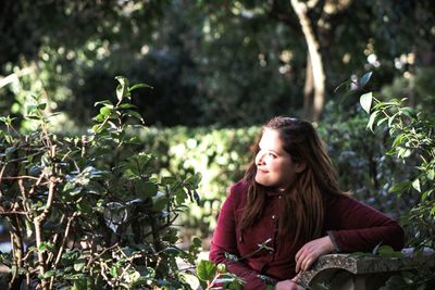 Smiling woman sitting amidst plants on sunny day