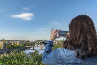 Rear view of woman photographing in city against blue sky