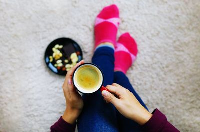 Top view of female hands holding coffee cup on floor at home.